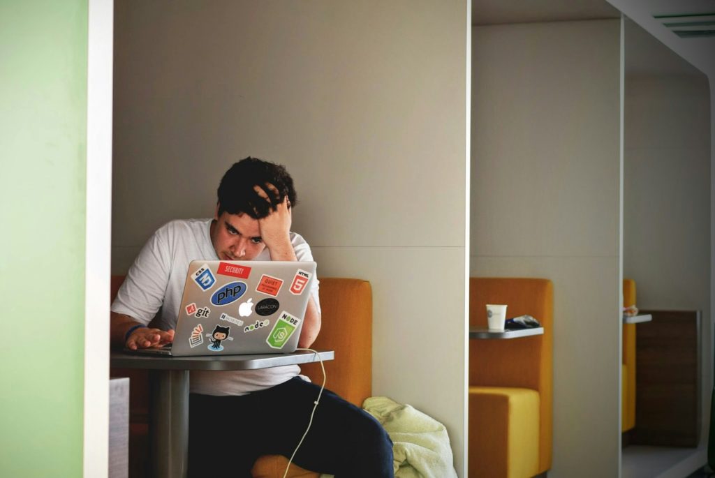 man wearing white top using MacBook looking like he's having a creative blocks