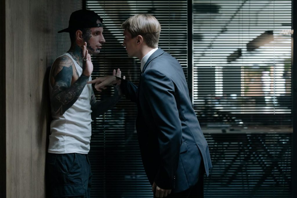 A businessman interrogating a tattooed suspect in an office environment, conveying tension.